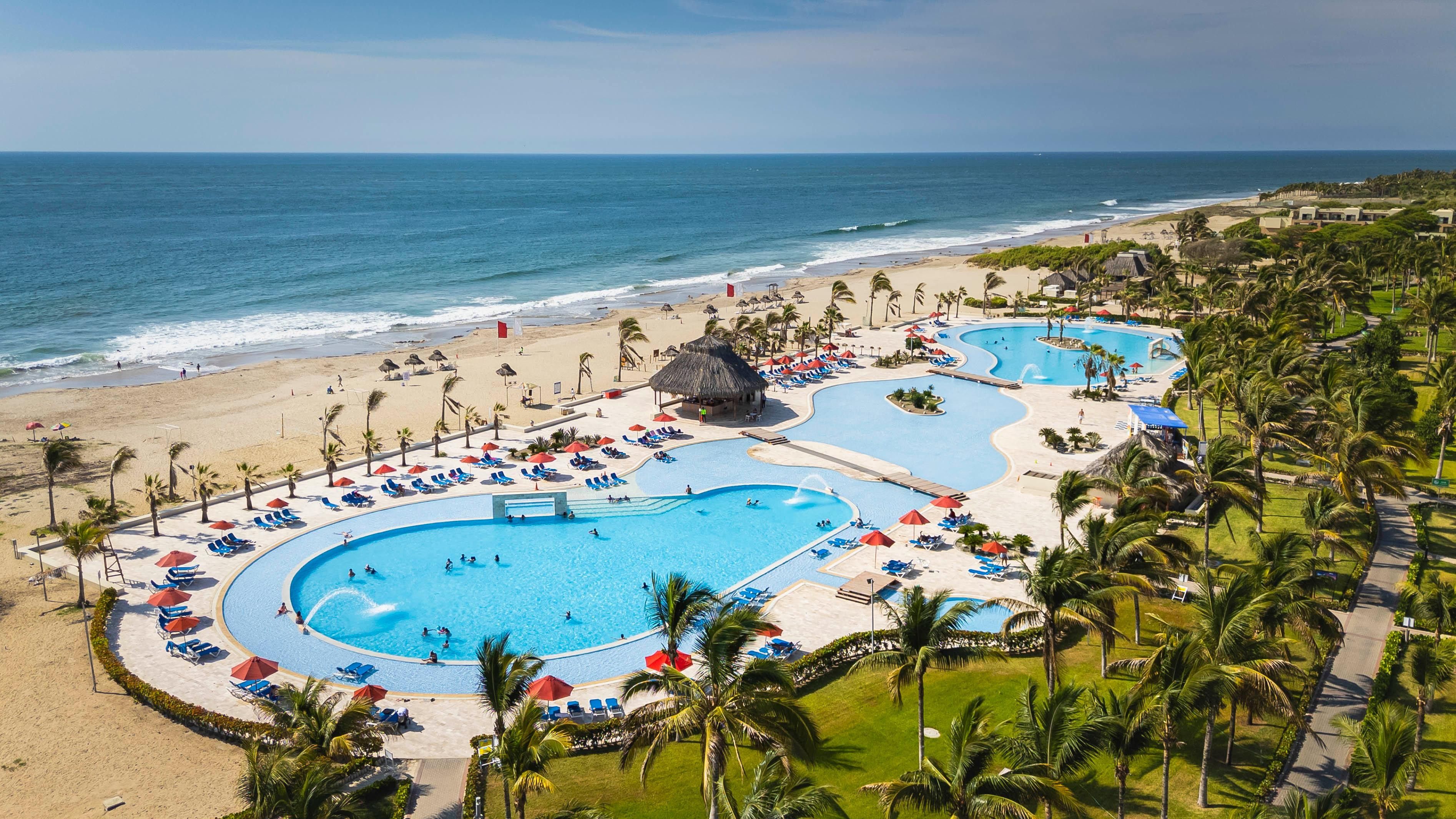 A resort with multiple swimming pools, a beach, and palm trees.