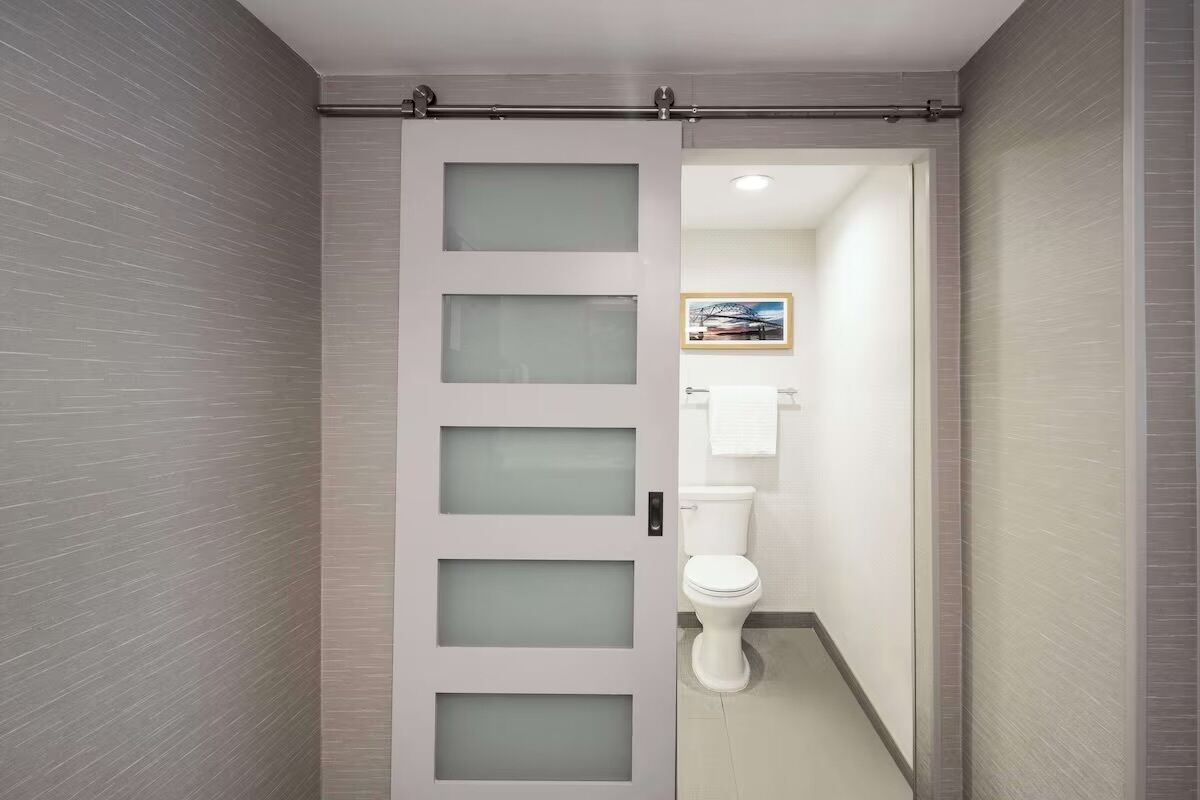 A modern bathroom with a frosted glass door, a toilet, and a framed picture on the wall.