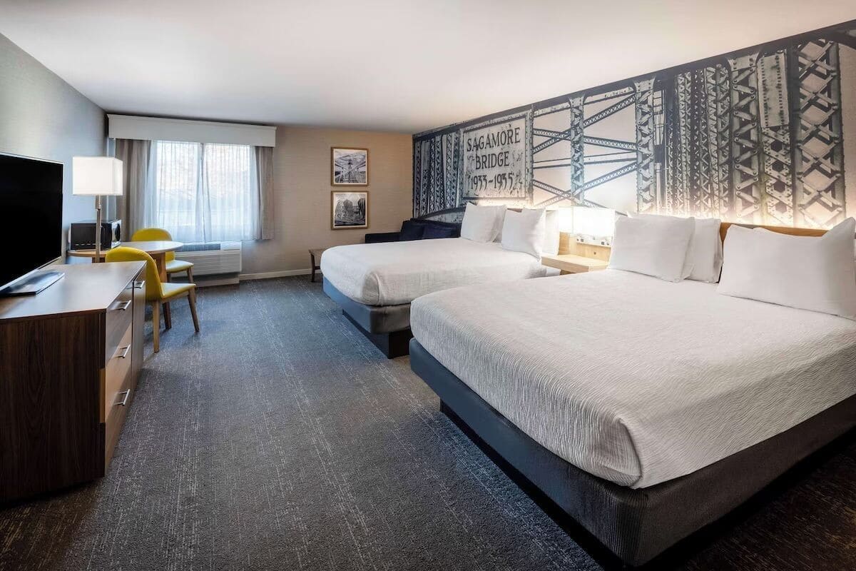 A hotel room with two beds, a desk, a TV, and a window with curtains.