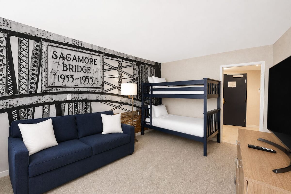 A room with a bunk bed, a sofa, a lamp, and a wall with a historical bridge sign.
