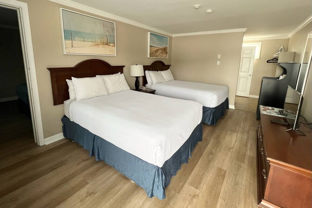 A hotel room with two beds, wooden headboards, a dresser, and a desk with a lamp.