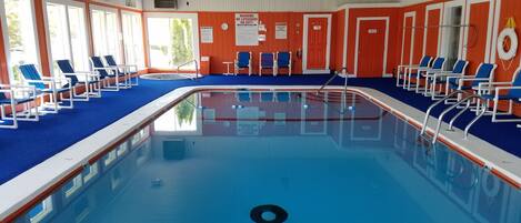Une piscine intérieure à l’eau bleue, entourée de murs orange et de portes blanches.