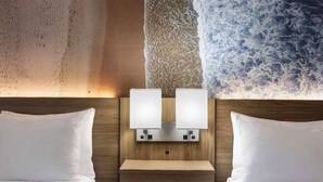 A hotel room with a wooden headboard, two bedside lamps, a wooden nightstand, and a textured wall. - Cape Cod Family Resort and Parks (West Yarmouth)