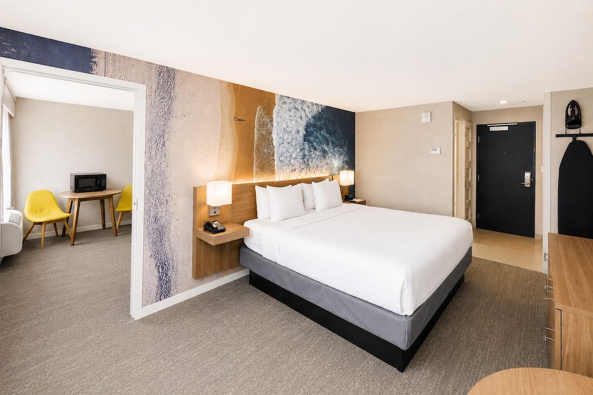 A hotel room with a bed, bedside tables, a desk with a chair, and a door.