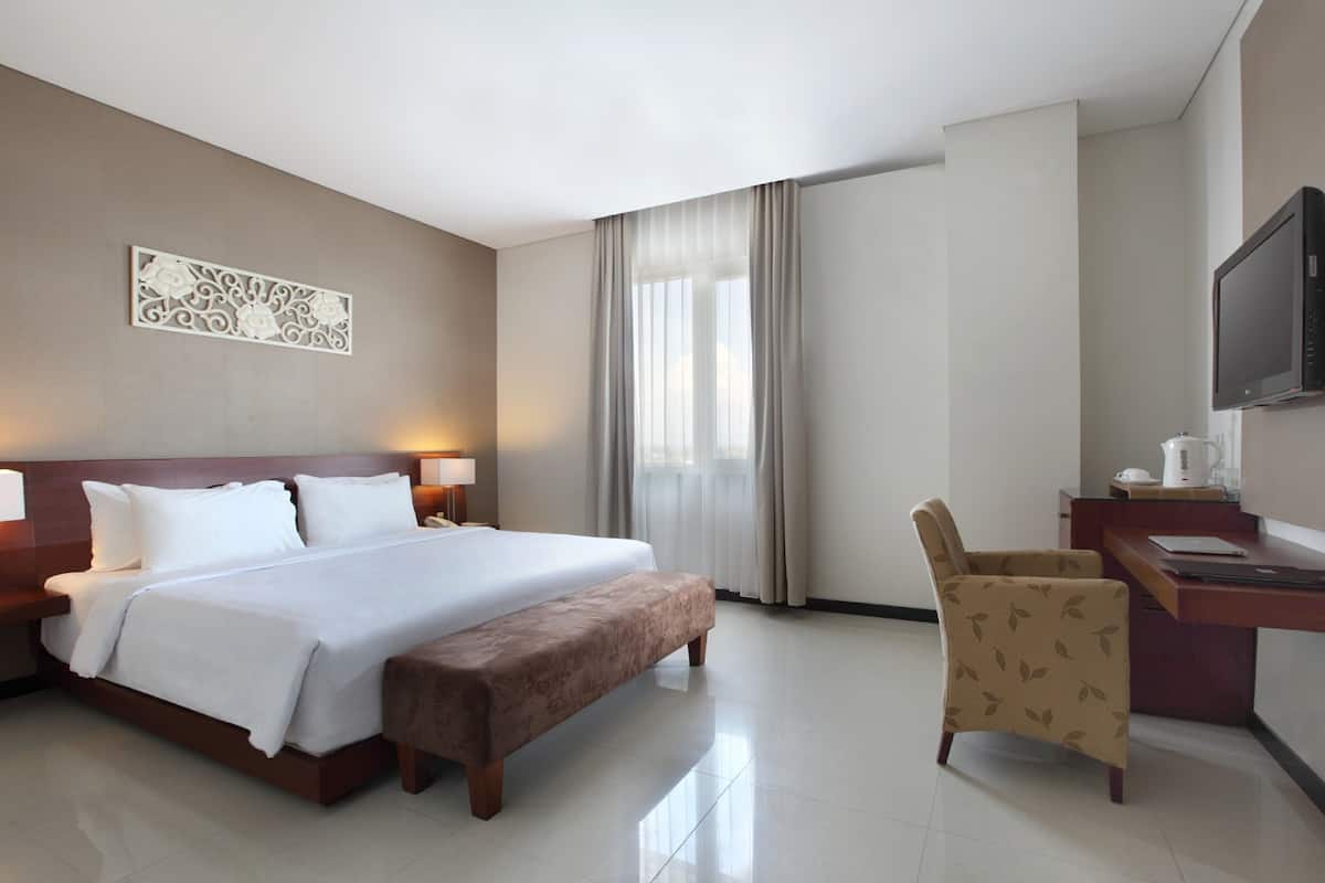 Una habitación de hotel con una cama grande, un escritorio con silla, televisión y ventana con cortinas.
