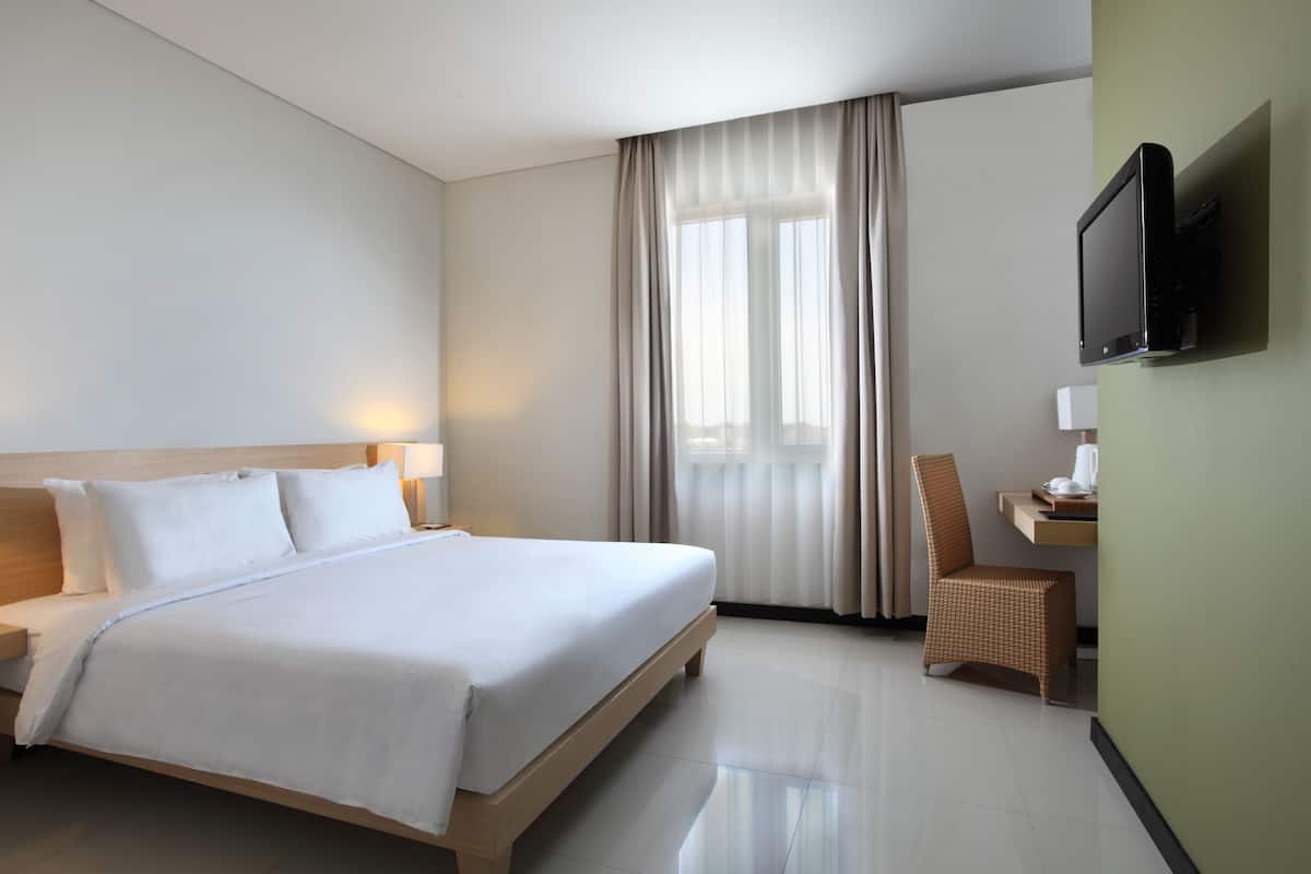 Una habitación de hotel con una cama grande, un escritorio con silla, un televisor montado en la pared y una ventana con cortinas.
