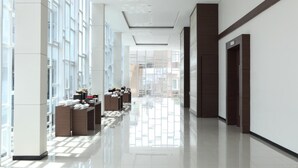 A modern hotel corridor with large windows, a clean floor, and a reception area with a counter and seating. - Hotel Santika Bengkulu (Bengkulu)