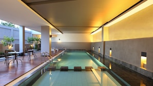 A modern indoor swimming pool with a wooden deck area, seating, and ambient lighting. - Hotel Santika Bengkulu (Bengkulu)