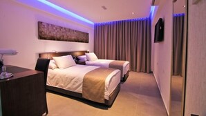 A hotel room with two beds, a desk, a flat-screen TV, and a large window with curtains. - Achilleos City Hotel (Larnaca)