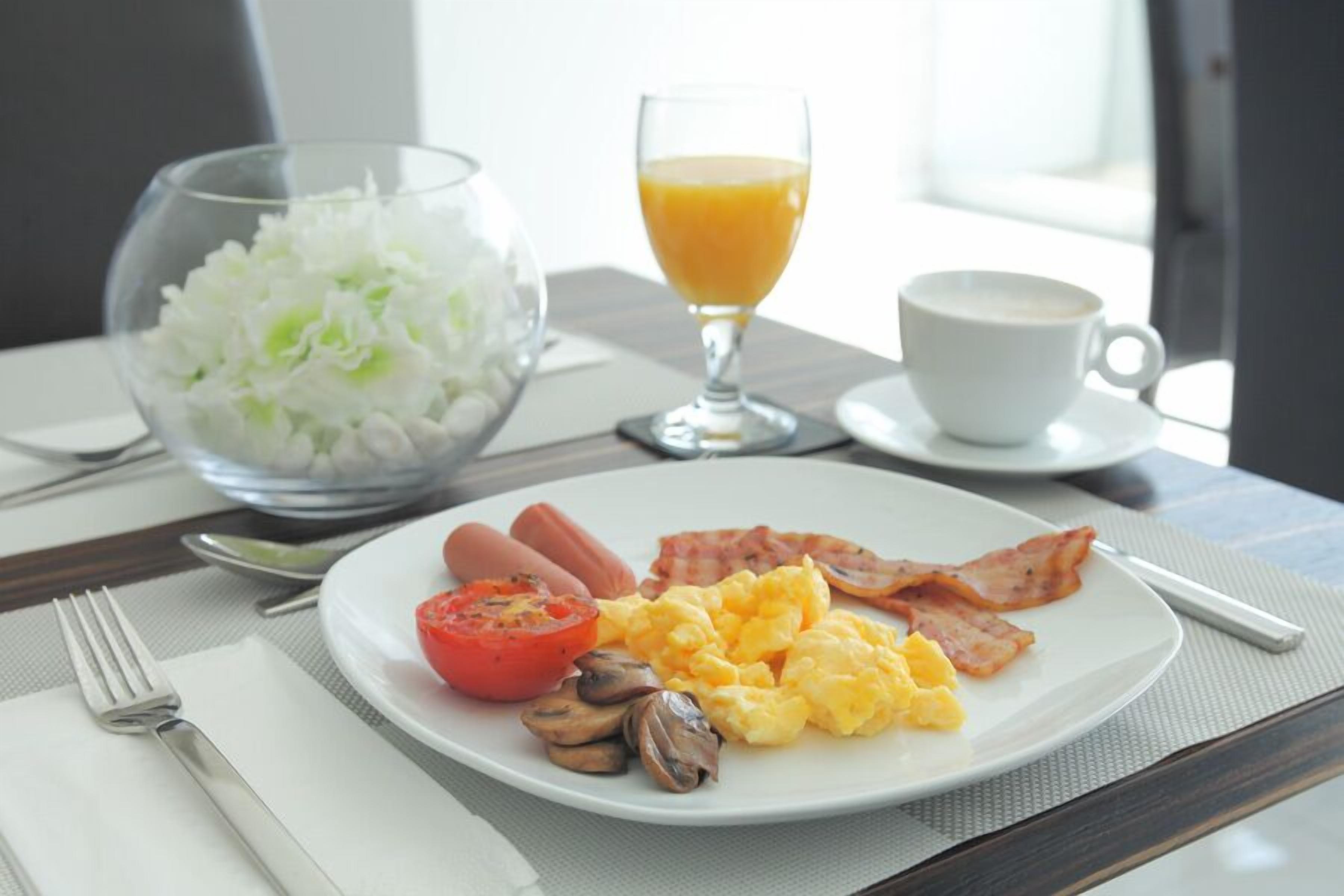 A breakfast plate with eggs, bacon, tomatoes, and mushrooms, a glass of orange juice, and a bowl of white flowers.