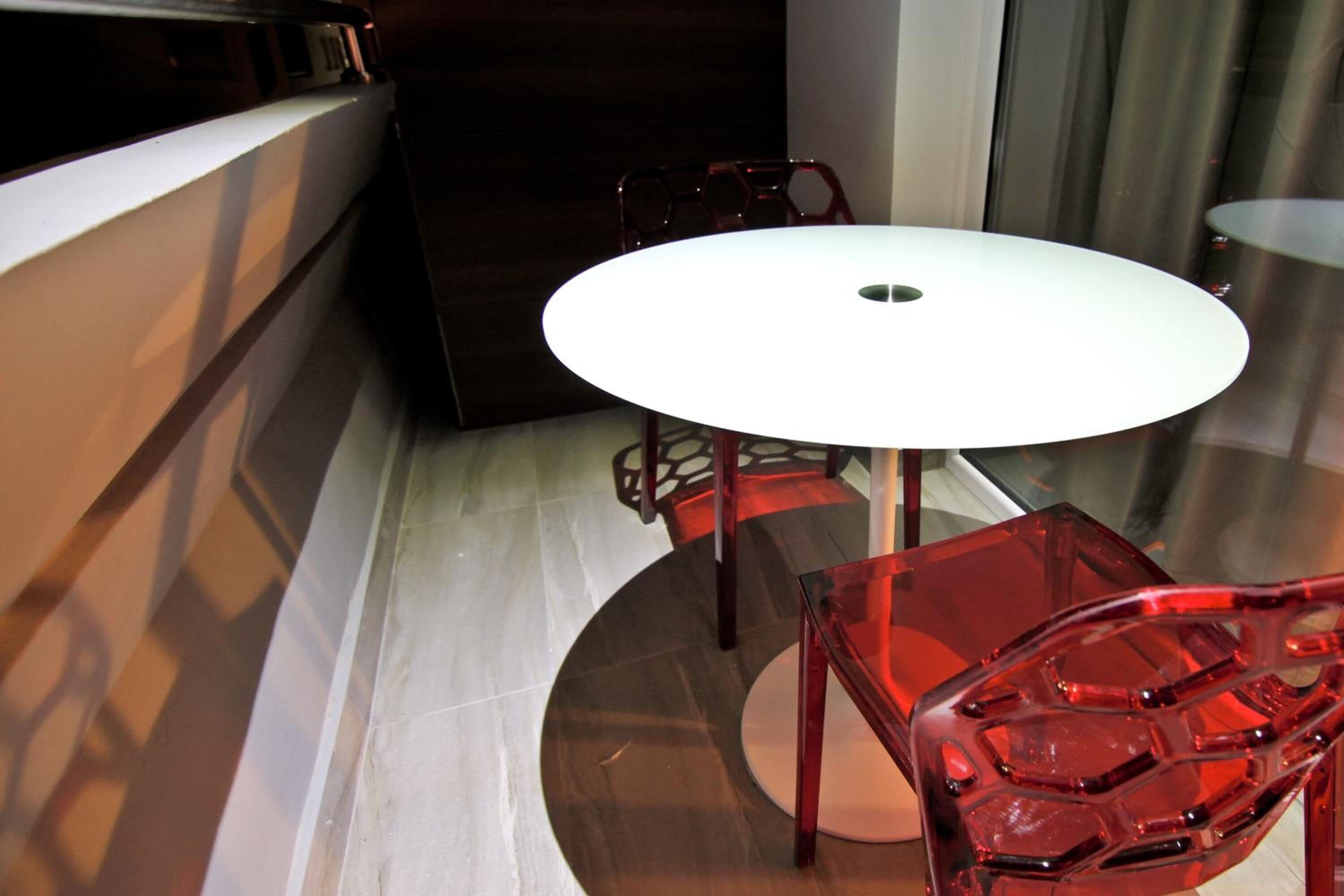 Quarto moderno com uma mesa redonda branca, cadeiras vermelhas e um armário de madeira escura.