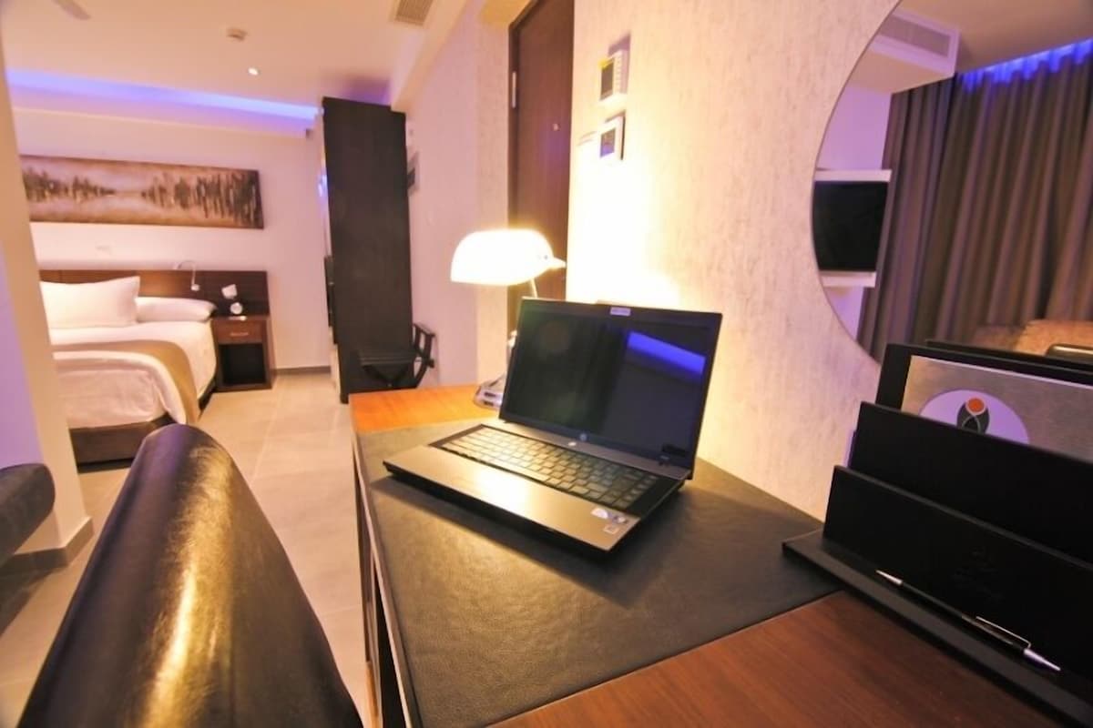 A hotel room with a bed, a desk with a laptop, a lamp, and a TV.