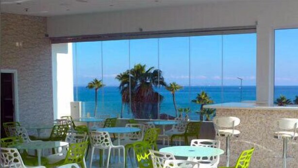 A hotel lobby with a large window overlooking the ocean, featuring a pool and outdoor seating area. - Achilleos City Hotel (Larnaca)