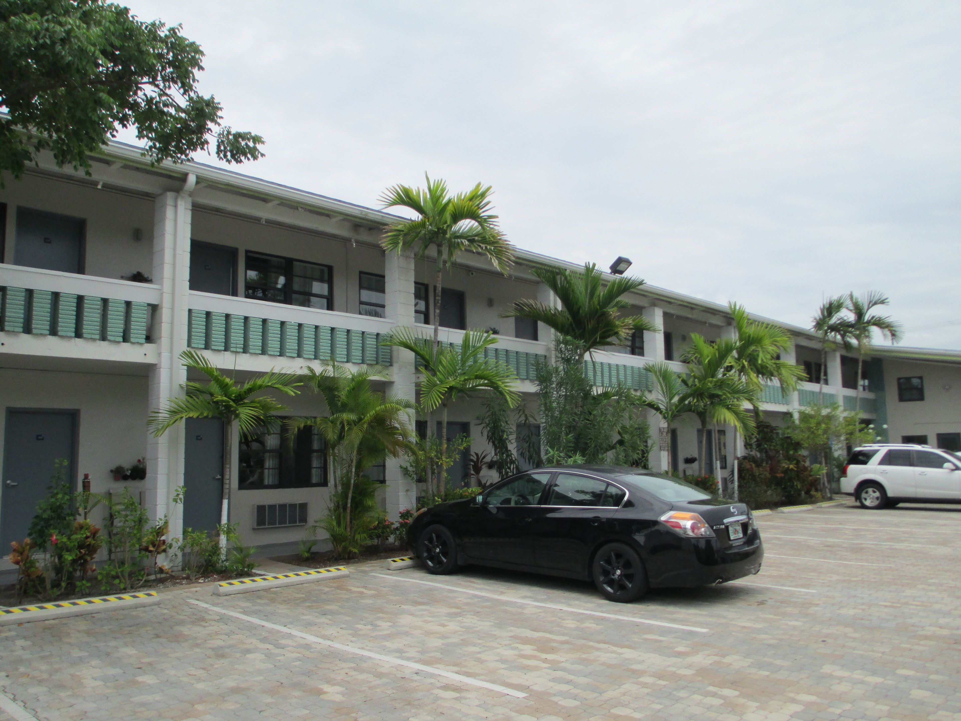 A multi-story hotel with a parking lot, featuring a black car parked in front.