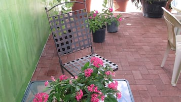 A glass table with a chair and potted plants on a brick patio.