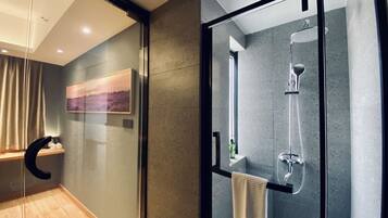 A modern bathroom with a glass shower enclosure, a wooden floor, and a painting on the wall.