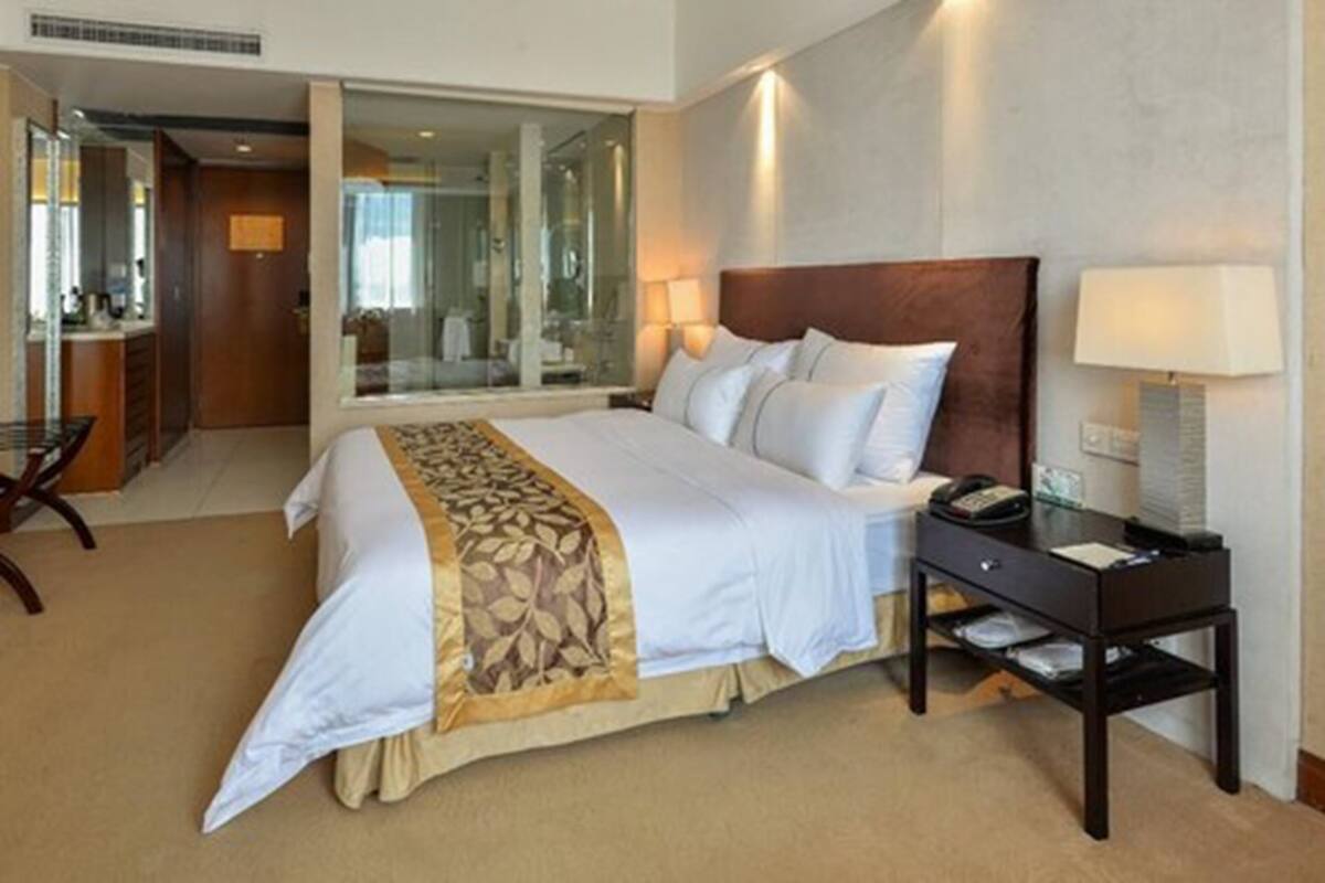 A hotel room with a large bed, a bedside table with a lamp, a mirror, and a view of a bathroom.