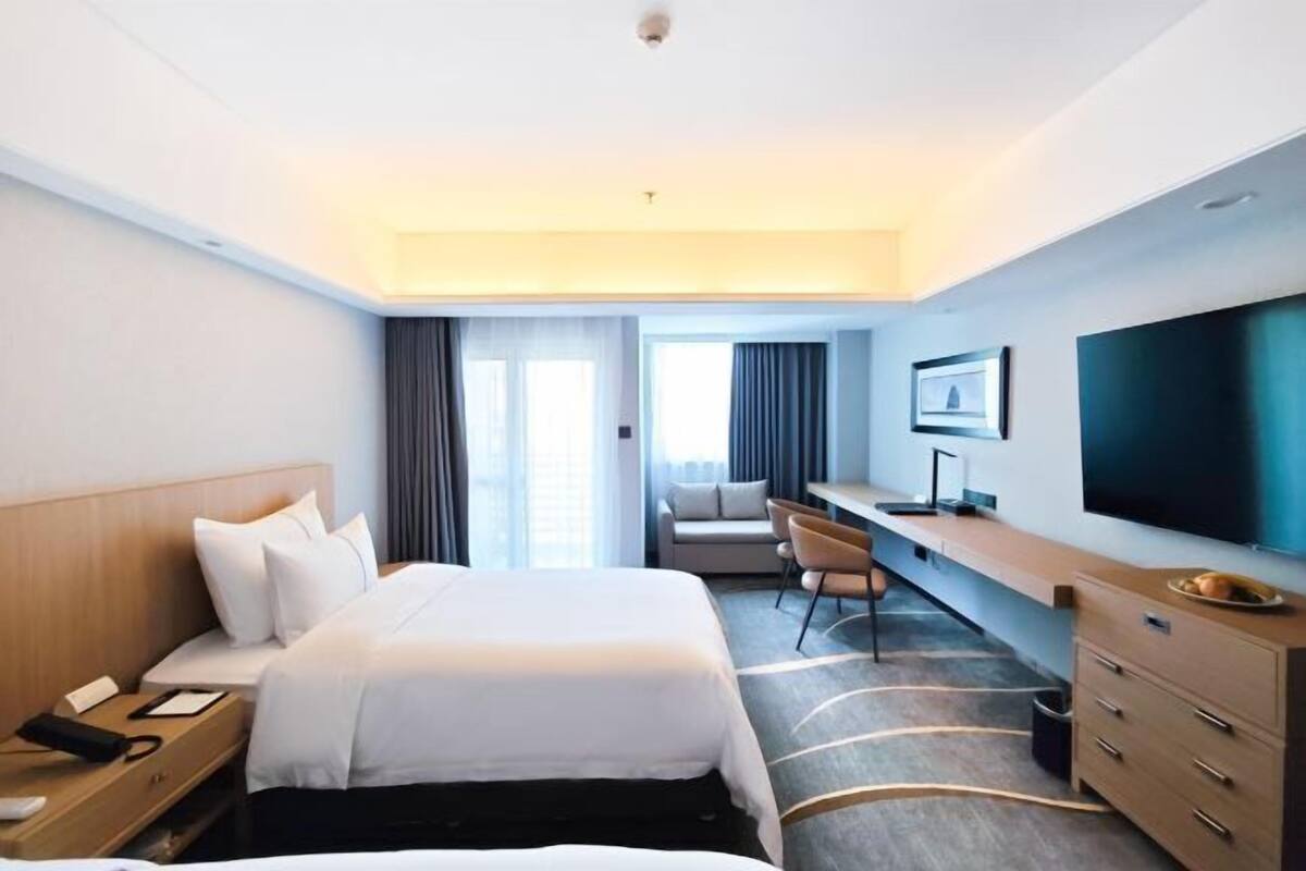 A hotel room with a bed, desk, TV, and a view of the city.