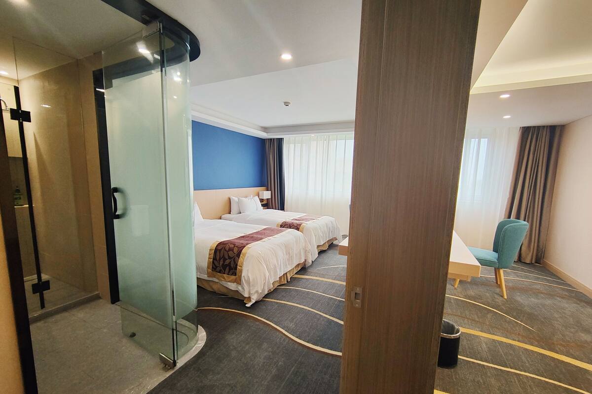 A hotel room with two beds, a glass partition, a desk, and a chair.