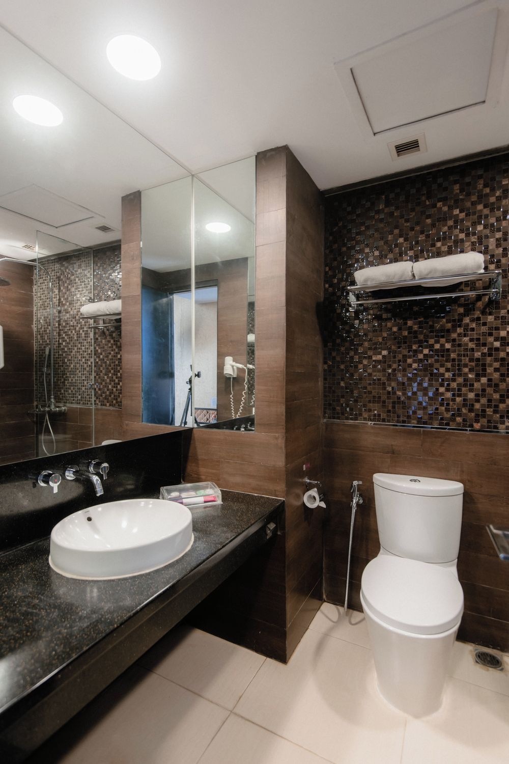 A modern bathroom with a large mirror, a sink, a toilet, and a shower area.