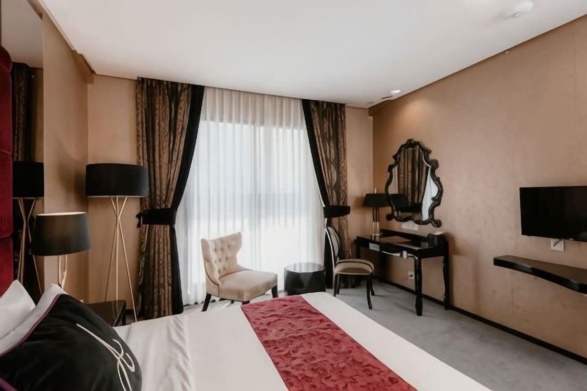 A hotel room with a bed, a desk, a chair, a television, and a large window with curtains.