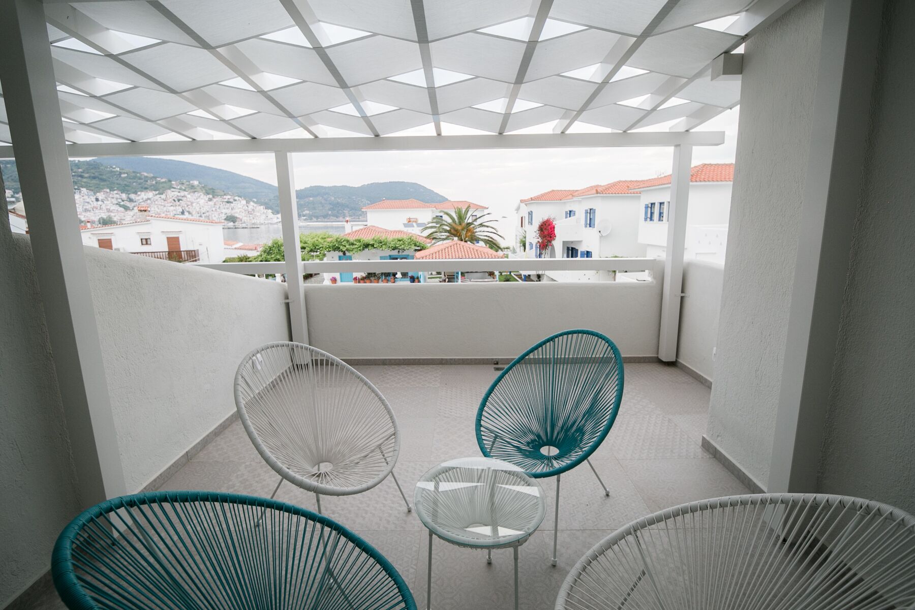 A balcony with white chairs and a view of a town with red-roofed buildings.