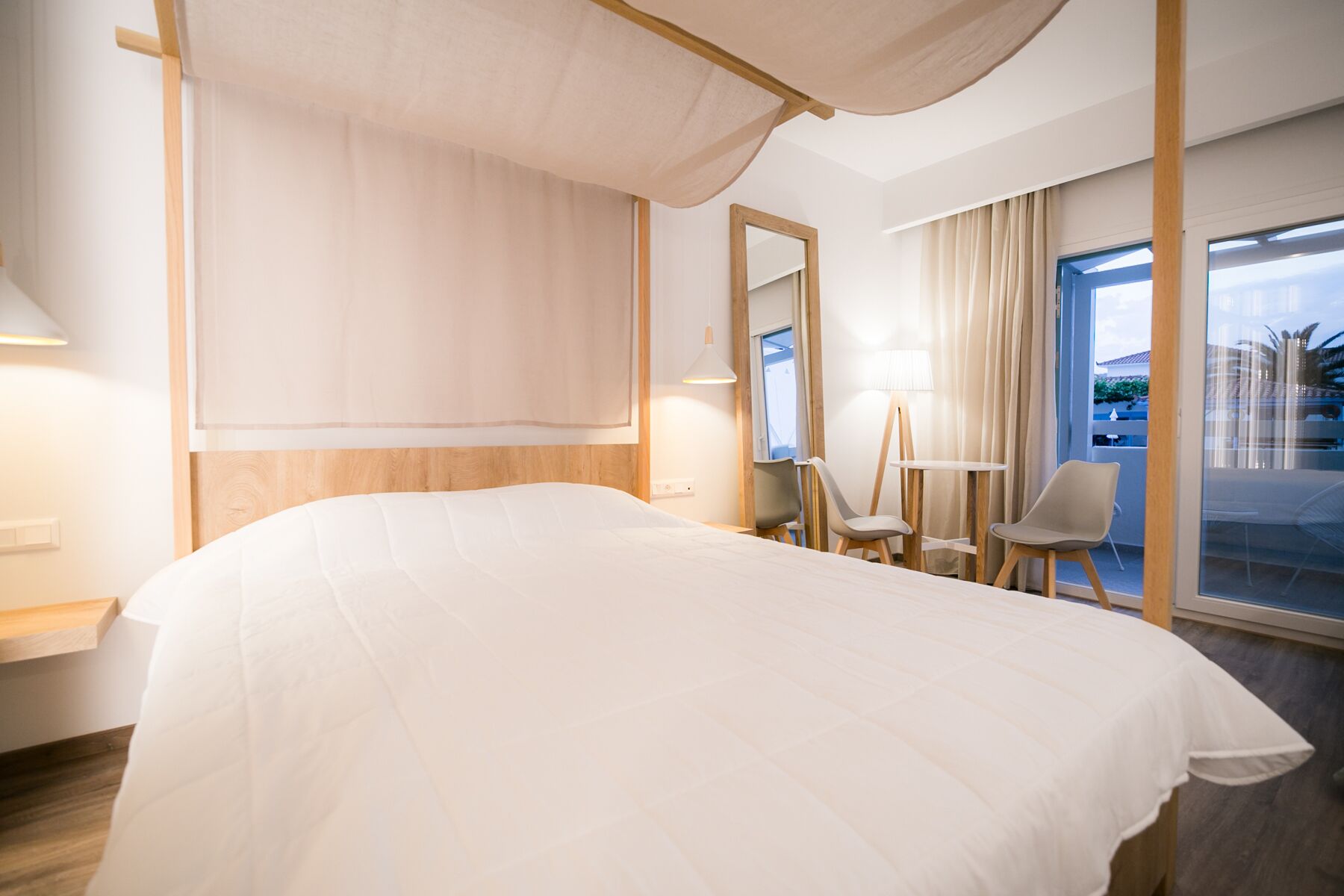 A modern hotel room with a large bed, a desk, a chair, and a balcony with a view.