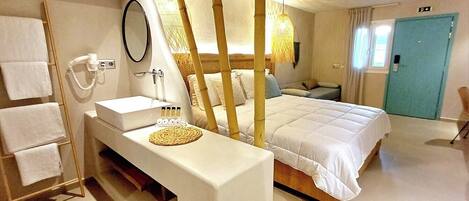 A hotel room with a bed, a bedside table with a mirror, a sink, and a towel rack.