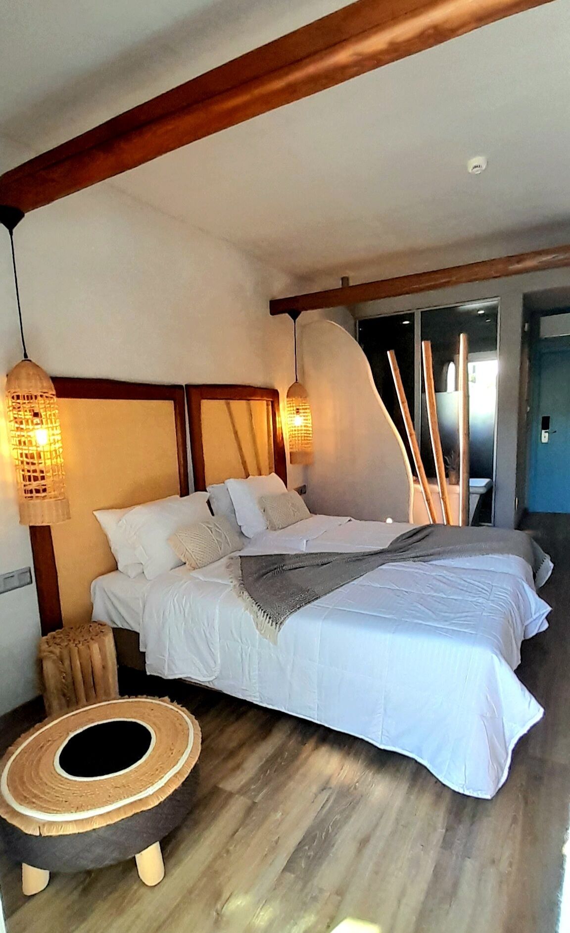 A bedroom with a large bed, a small stool, and a wall-mounted lamp.