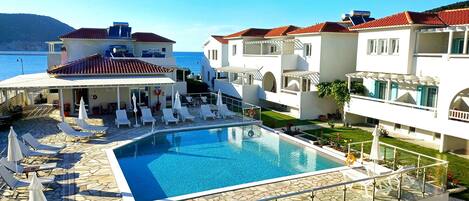 A pool area with lounge chairs and a view of the sea.