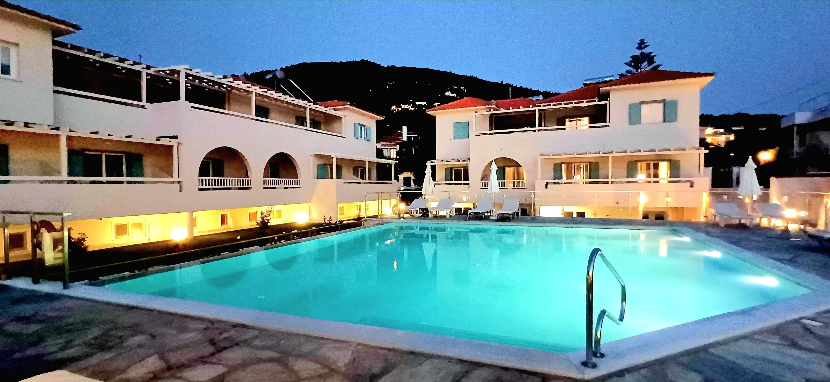 Una piscina con una escalera metálica, rodeada de edificios con balcones y mobiliario exterior.