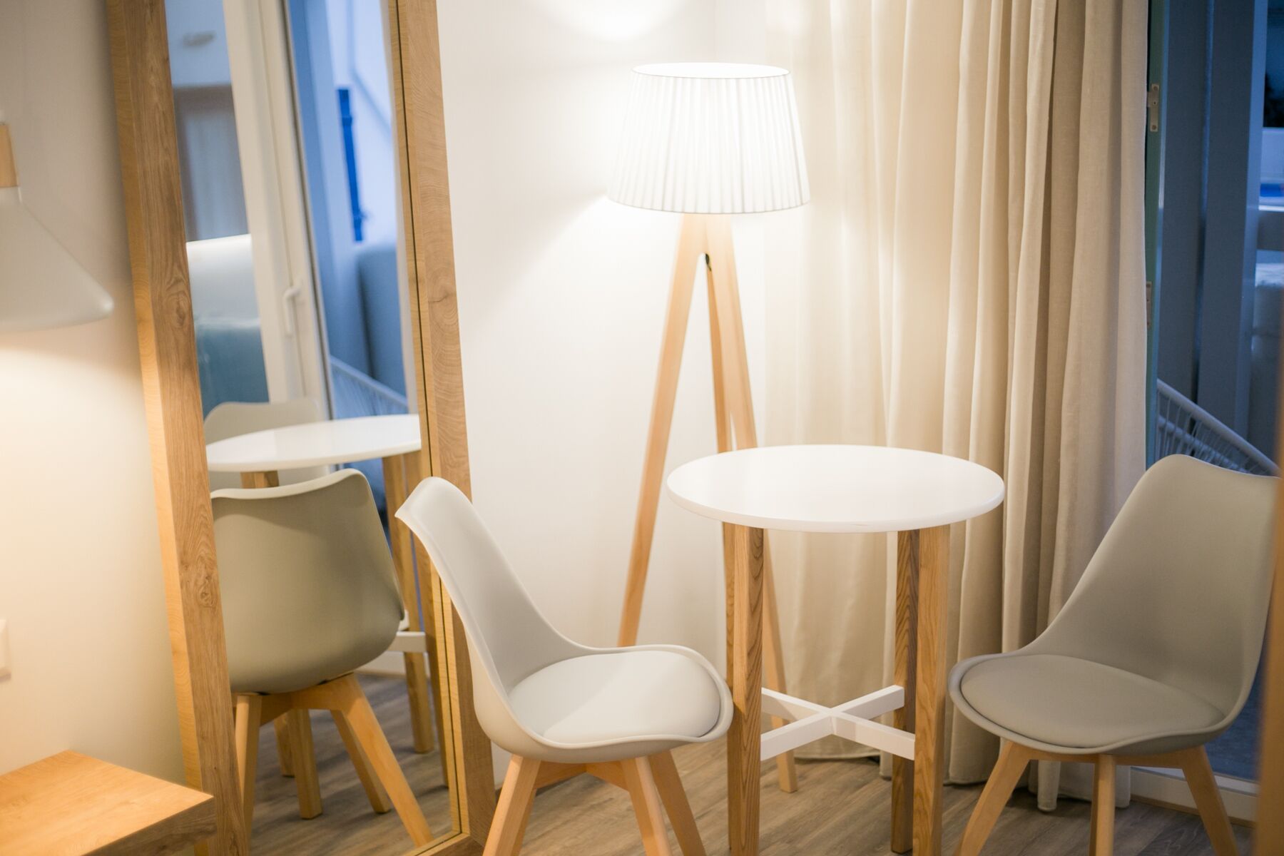 Une chambre d’hôtel moderne avec une table ronde et deux chaises, un lampadaire et une vue sur la ville grâce à de grandes fenêtres.