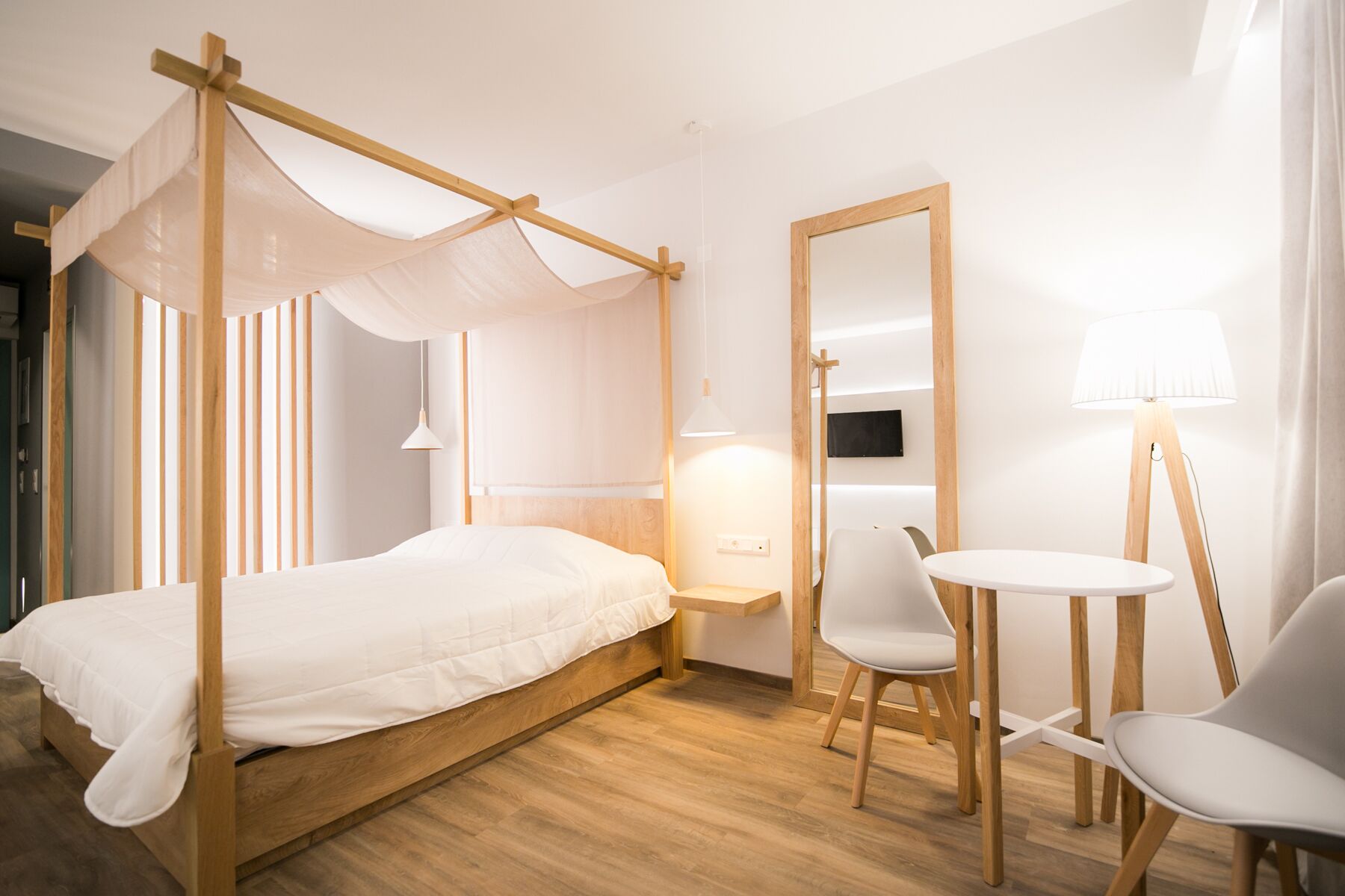 Una habitación con cama con dosel, una mesita pequeña con dos sillas, una mesita de noche y un espejo.