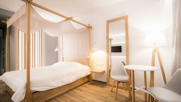 Una habitación con cama con dosel, una mesita pequeña con dos sillas, una mesita de noche y un espejo.