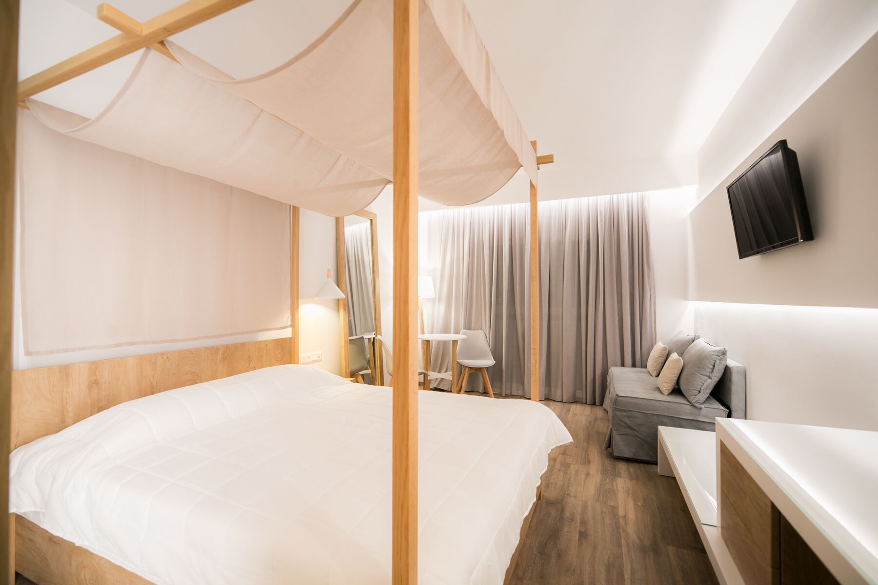 A modern hotel room with a large bed, a sofa, a TV, and a desk.