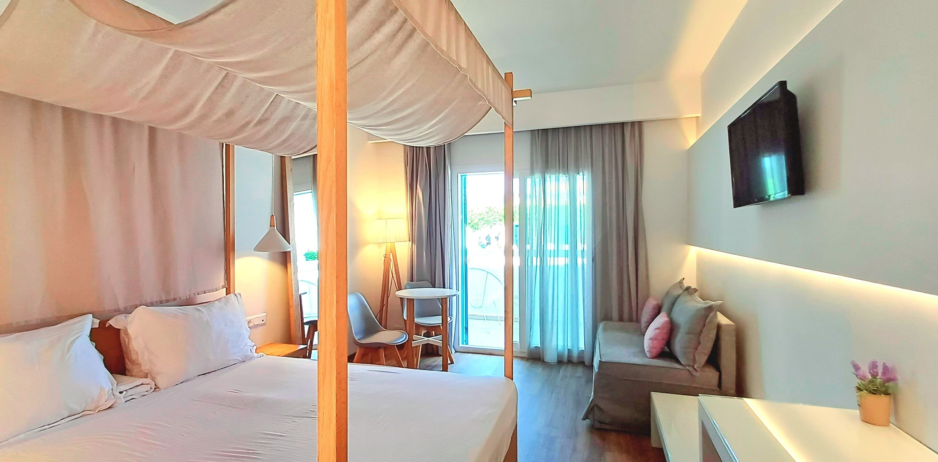 Habitación de hotel con cama con dosel, sofá, mesita y televisor montado en la pared.