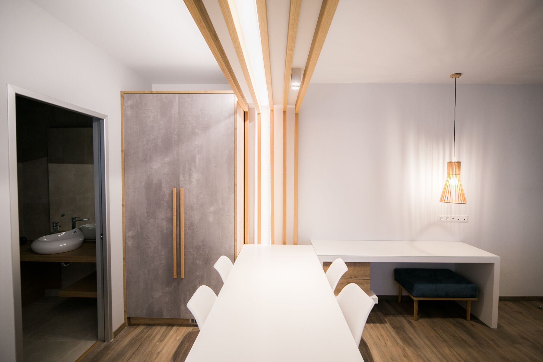Un espace de salle à manger moderne avec une table blanche, des poutres en bois et un luminaire suspendu.