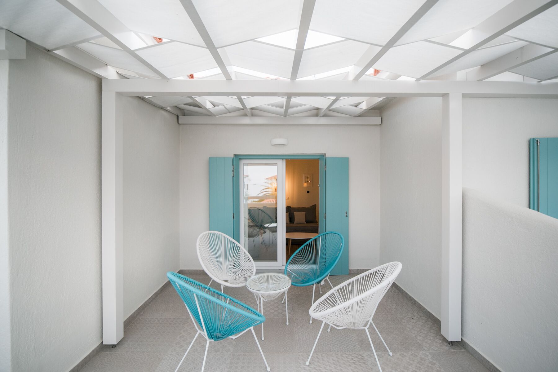Un interior moderno con techo de tragaluces, paredes blancas y una puerta que da a una habitación con sofá y sillones.