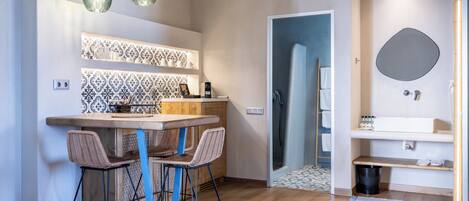 A modern kitchen with a bar area, two wicker chairs, pendant lights, patterned backsplash, and a wooden floor.