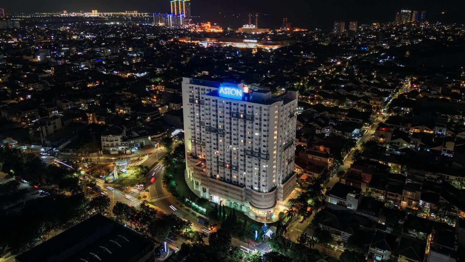 A high-rise hotel with a prominent 'Aston' sign, surrounded by a dense urban area at night.