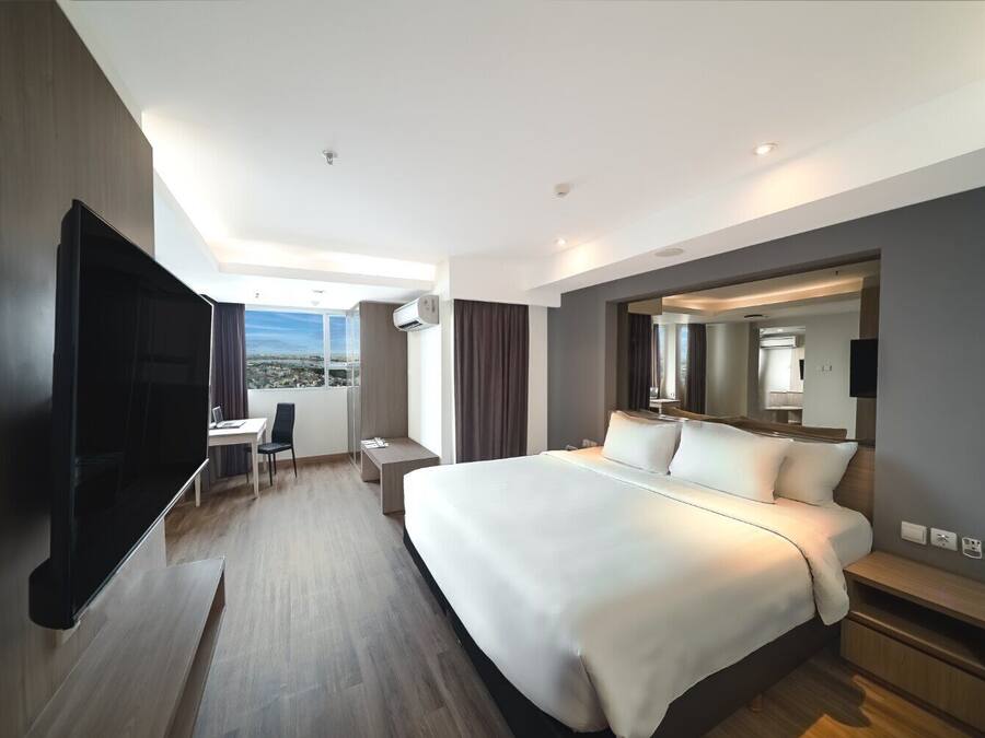 A modern hotel room with a large bed, a desk, and a TV.