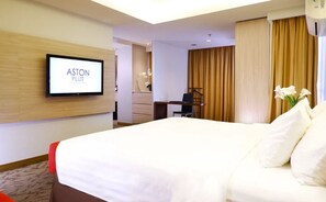 A hotel room with a large bed, a desk, a chair, a television mounted on the wall, and a window with curtains. - Aston Pluit Hotel & Residence (Jakarta)