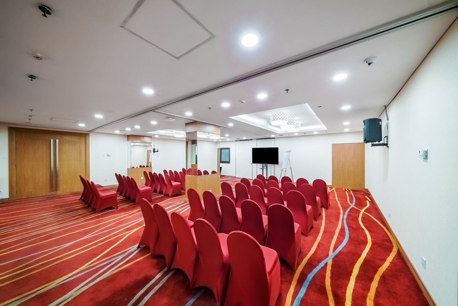 Ein Konferenzraum mit roten Sitzreihen, einer großen Leinwand und einem Teppichboden.
