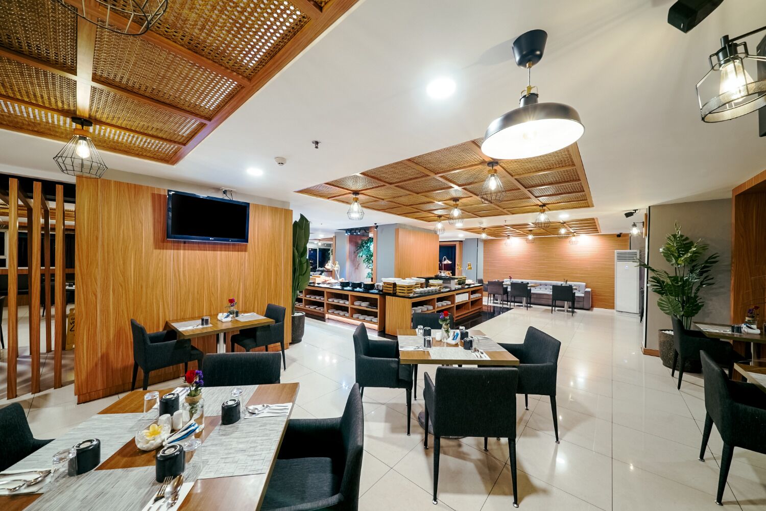Un restaurante moderno con paneles de madera, sillas negras y una zona central de comedor con mesas para dos.