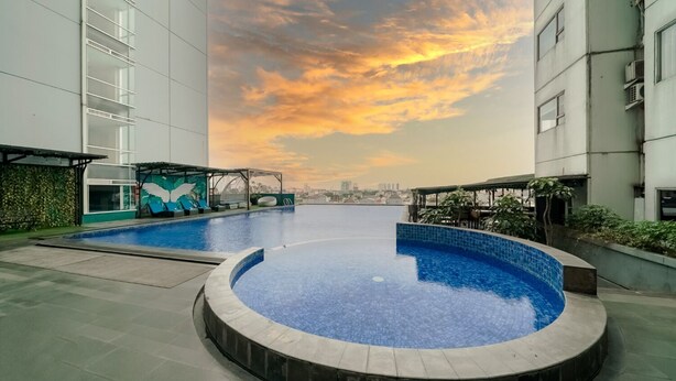 Una piscina en la azotea con vista a un paisaje urbano, rodeada de edificios modernos.