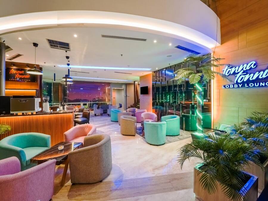 Un salón de estar en el vestíbulo con techo curvo, zonas de descanso, un mostrador de recepción y un letrero de neón.