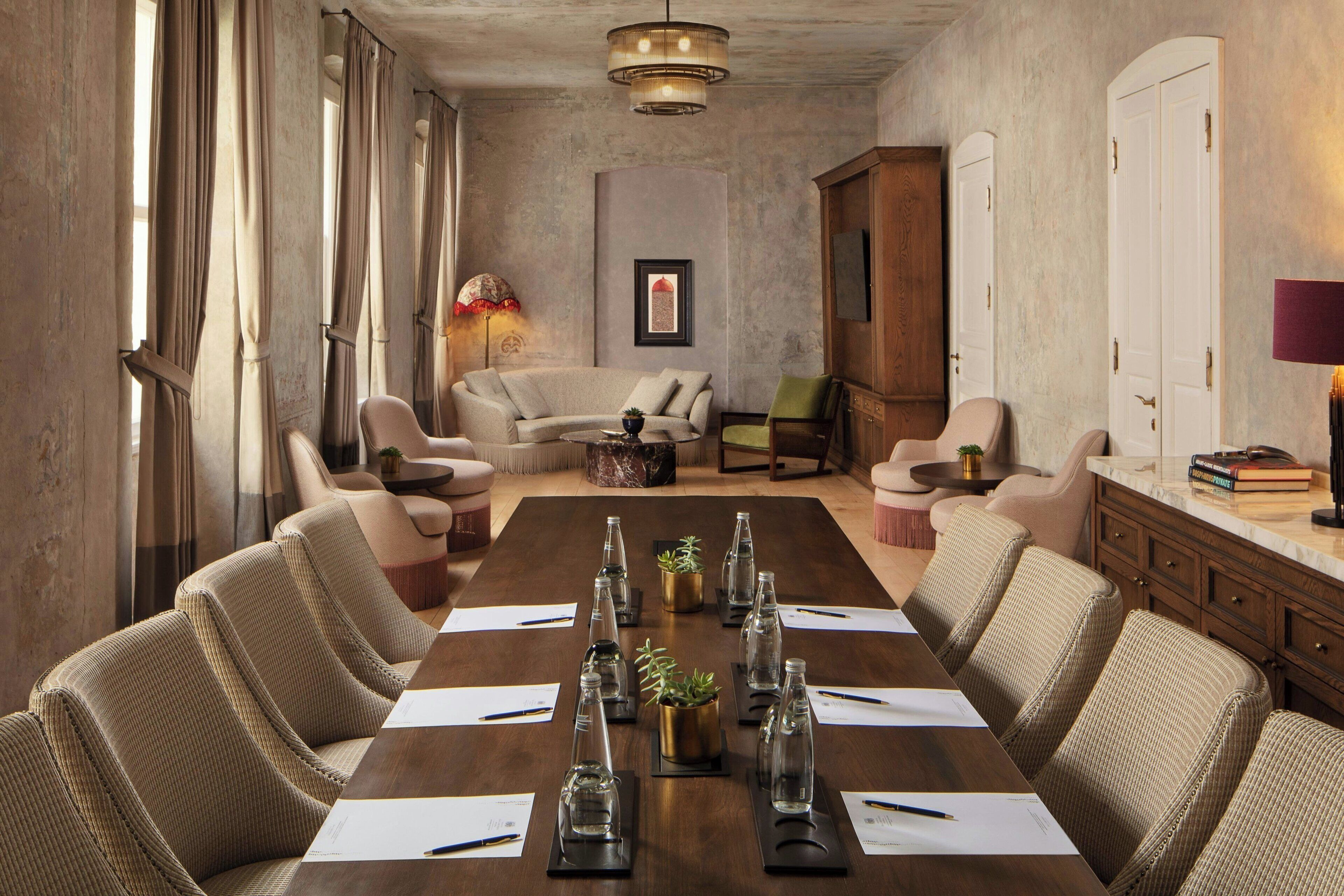 A conference room with a long table, chairs, and a sofa. There are plants on the table and a lamp on the wall.
