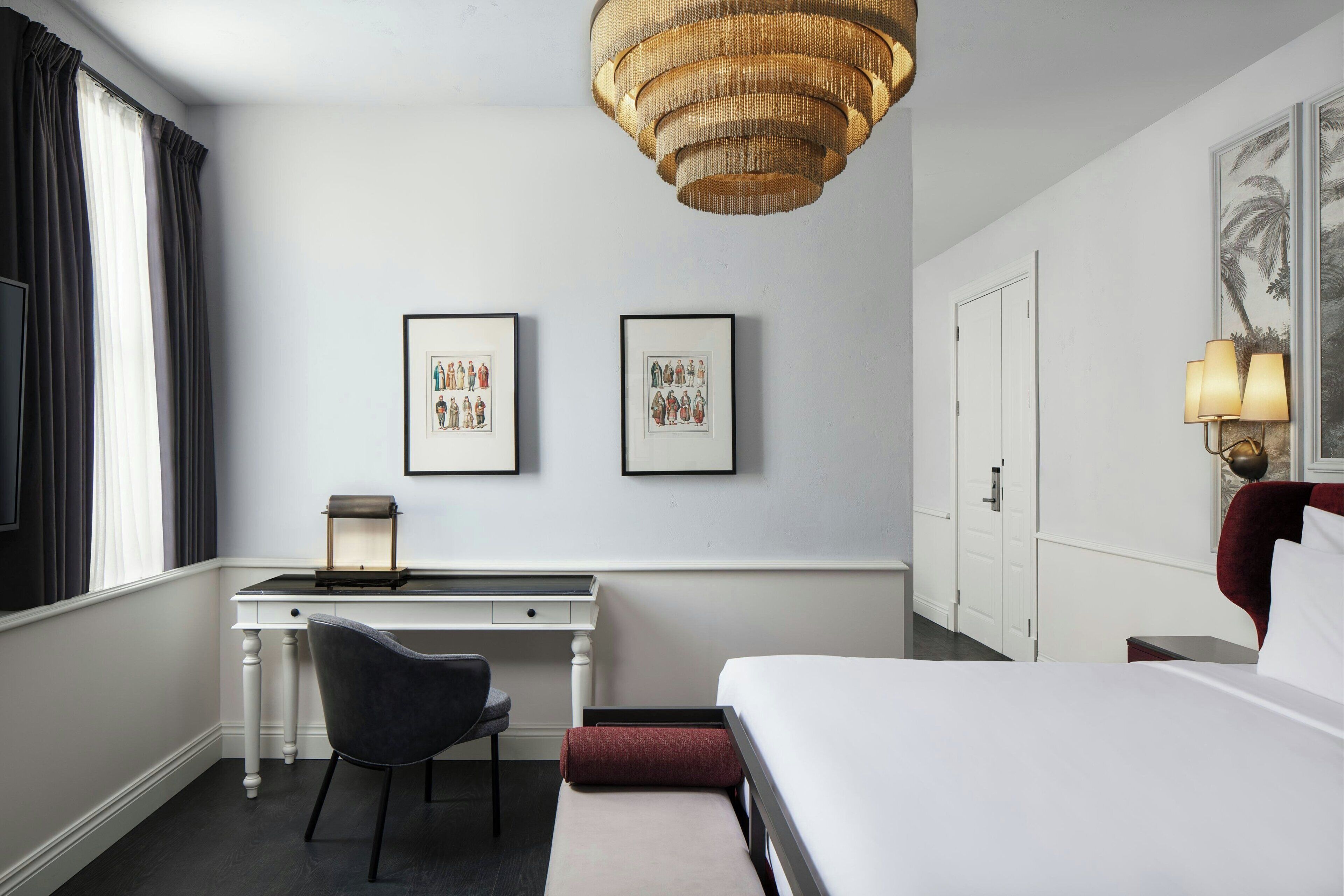 A hotel room with a bed, desk, chair, and artwork on the wall.