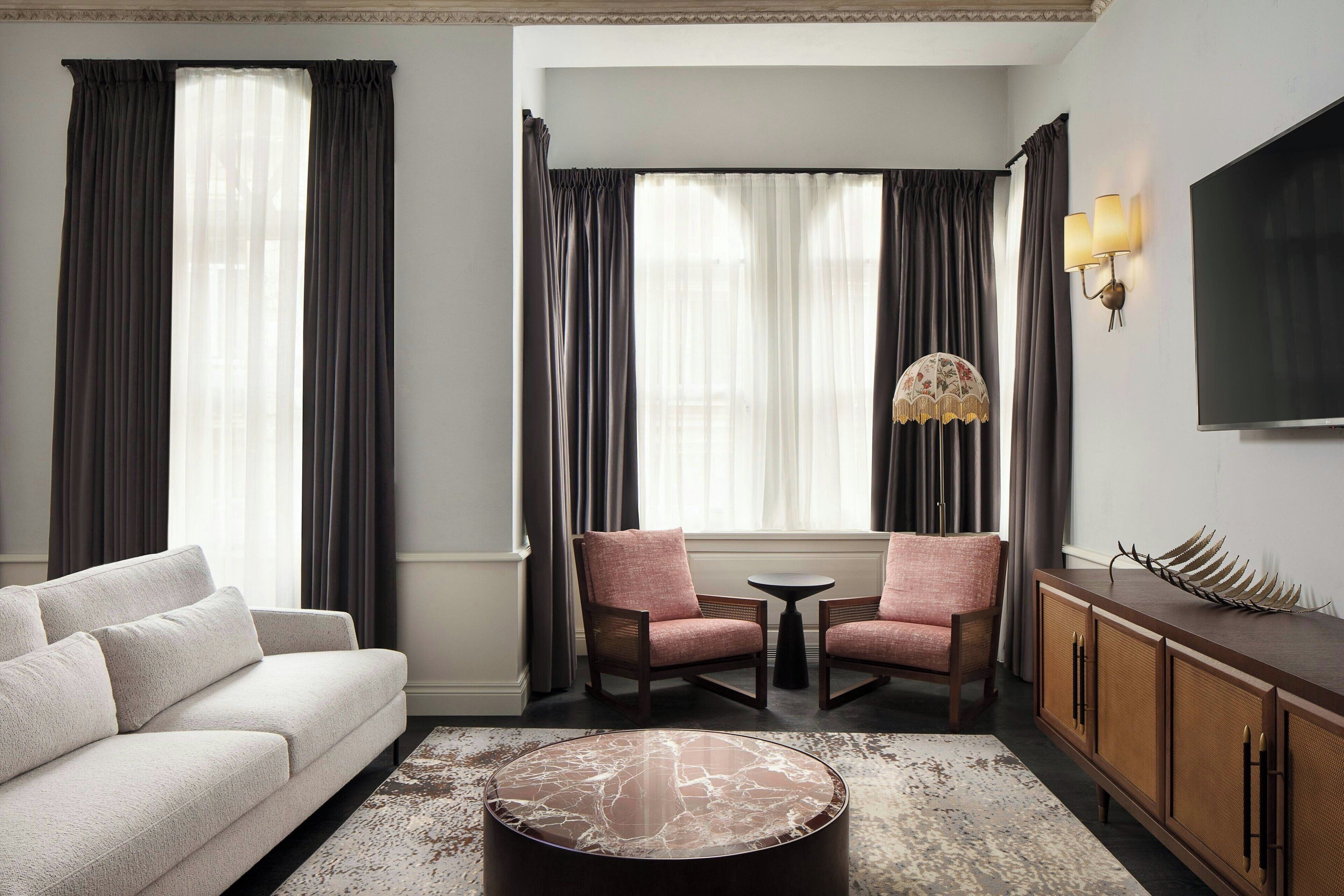 A hotel room with a sofa, two armchairs, a coffee table, a TV, and a decorative lamp.