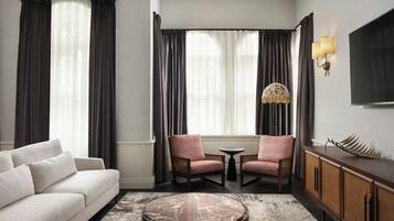 A hotel room with a sofa, two armchairs, a coffee table, a TV, and a decorative lamp.